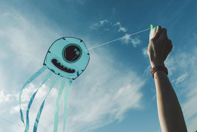 Cropped hand flying kite against sky