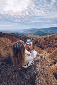 Man photographing on rock against sky