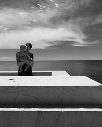 Man on retaining wall by sea against sky