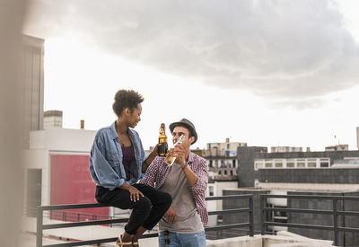 Full length of young man drinking water in city against sky