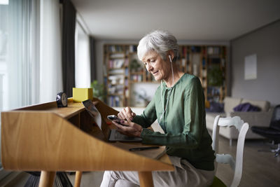 Active senior listening music while sitting on chair at home