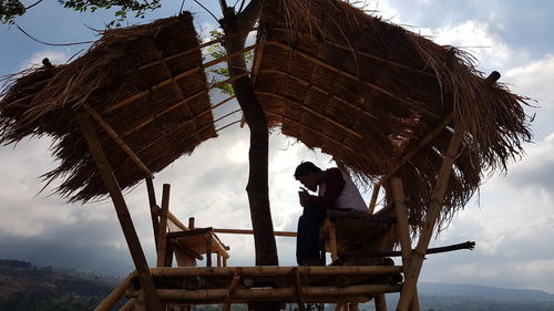 Man smoking cigarette while sitting in hut against sky