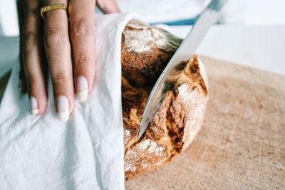 Cropped hand on woman cutting bread on cutting board