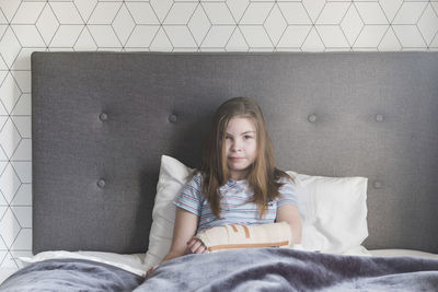 Close up of a young girl sitting in bed at home with a broken arm