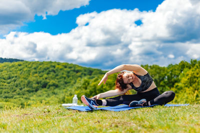 Young woman sitting on field against sky