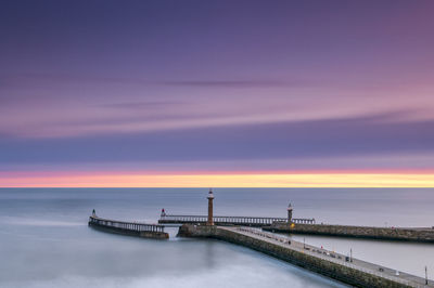 Lighthouses on pier over sea against cloudy sky during sunset