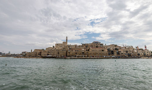 View of buildings by sea against cloudy sky