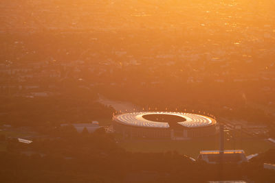 High angle view of illuminated ferris wheel against orange sky