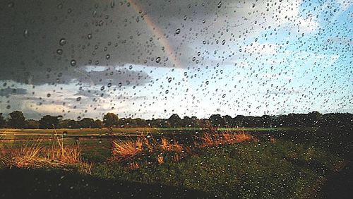 Raindrops on glass window against sky during rainy season