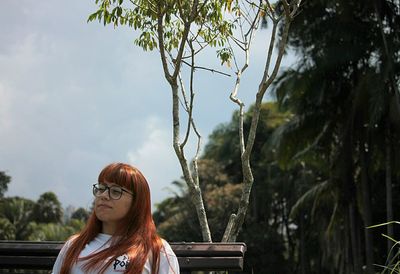 Low angle view of thoughtful young woman looking away while sitting on bench at park