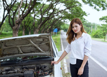 Smiling young woman standing by car