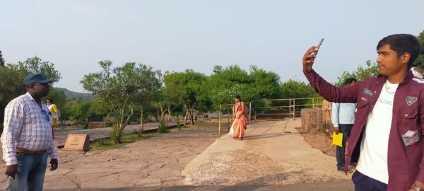 Man photographing with arms outstretched standing against sky