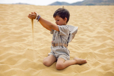 Portrait boy child traveler in a suit of an archaeologist and wearing hat sitting on sand in desert