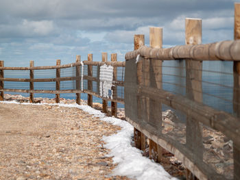 Fence on beach against sky during winter