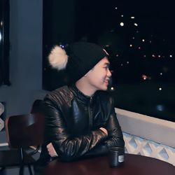 Smiling young man looking away while sitting by railing at night