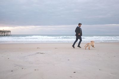 Man playing with dog at beach against clear sky