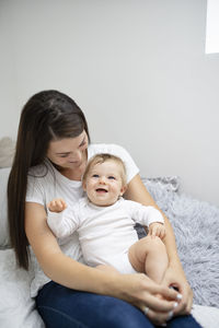 Portrait of smiling mother and daughter sitting on bed at home