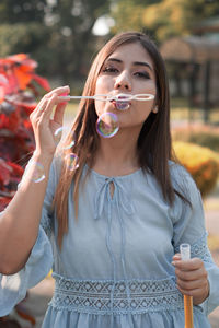 Beautiful young woman blowing bubbles while standing against plants