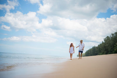 Man and woman walking at beach against sky