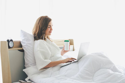 Young woman using phone while sitting on laptop