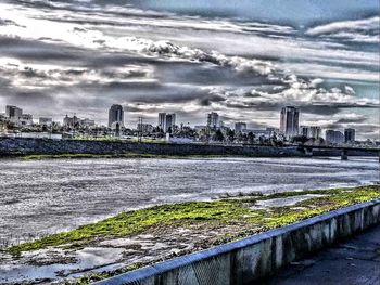 Bridge over river by buildings in city against sky