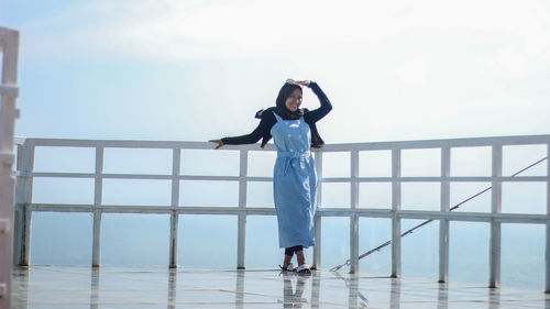 Woman standing by railing against clear blue sky