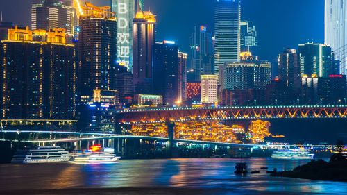 Illuminated bridge over river by buildings in city at night