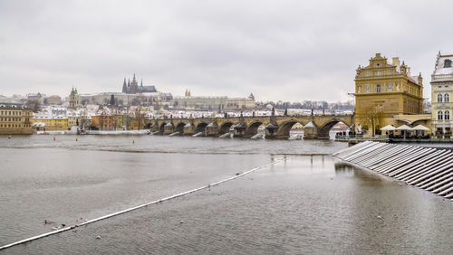 Bridge over river in city against cloudy sky