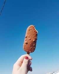 Cropped hand holding ice cream against clear blue sky