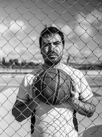 Portrait of young man looking through chainlink fence