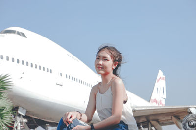 Smiling woman sitting against airplane
