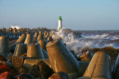 Lighthouse by sea against clear sky and waves splashing