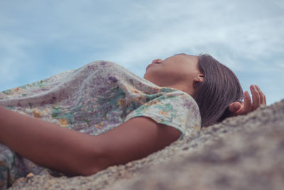 Midsection of woman lying on rock against sky