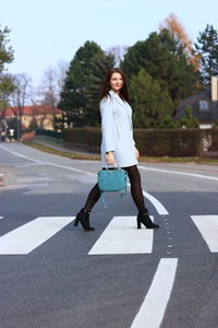 Full length portrait of smiling young woman crossing road