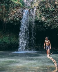 Full length of shirtless man standing on fallen tree over river