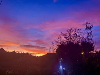 Silhouette trees against illuminated city during sunset