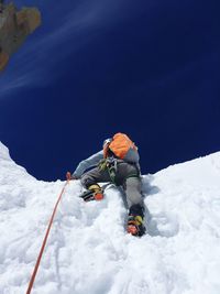 Low angle view of person with backpack climbing snowcapped mountain against blue sky