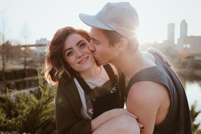 Young man kissing happy woman during sunset