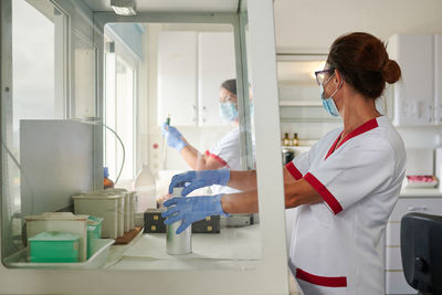 Side view of anonymous female scientists in uniforms and masks standing near table with medical tools in lab