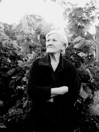 Mature woman with arms crossed looking away while standing against plants in park