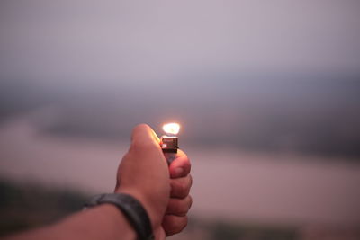 Midsection of person holding candle against sky during sunset