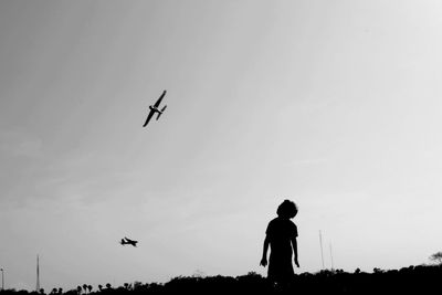 Low angle view of silhouette man flying airplane against sky