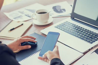 Midsection of woman with coffee analyzing graphs by laptop on table