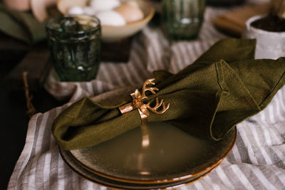 Green cloth napkin is secured with a golden ring in the form of a deer's head.