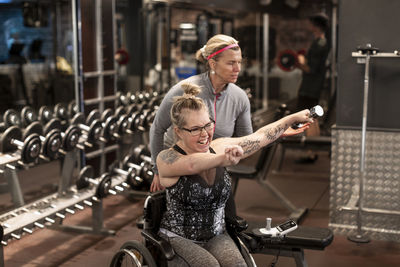 Happy woman on wheelchair training in gym with personal trainer