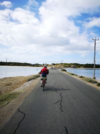 Rear view of man riding bicycle on road leading towards beach
