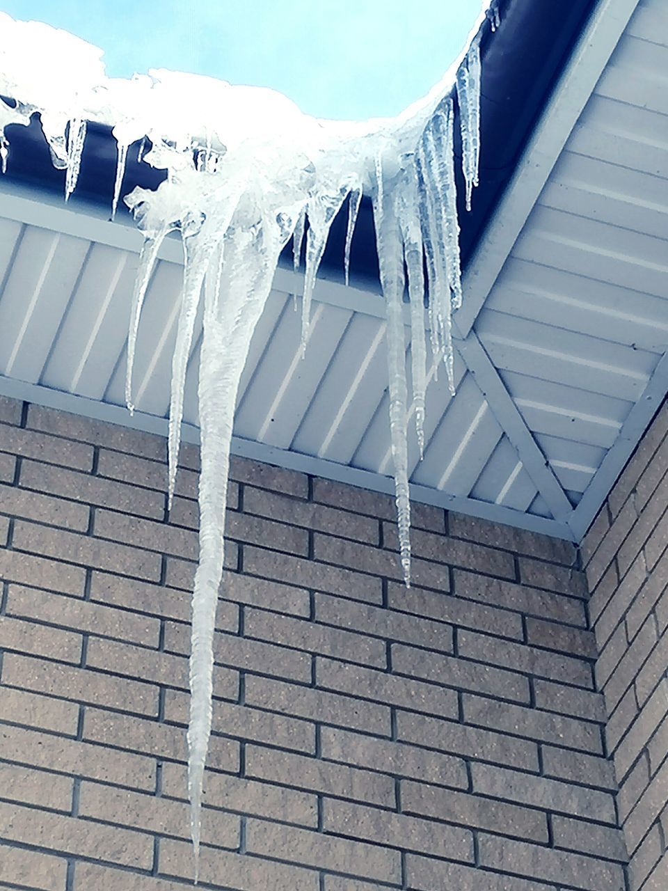 LOW ANGLE VIEW OF ICICLES ON ROOF AGAINST BUILDING