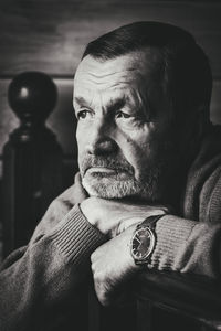 Senior man looking away while leaning on wooden railing at home