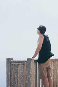 Rear view of man standing by railing against clear sky