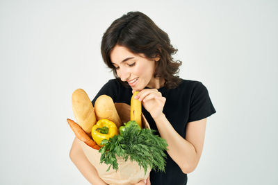 Young woman holding groceries against white background